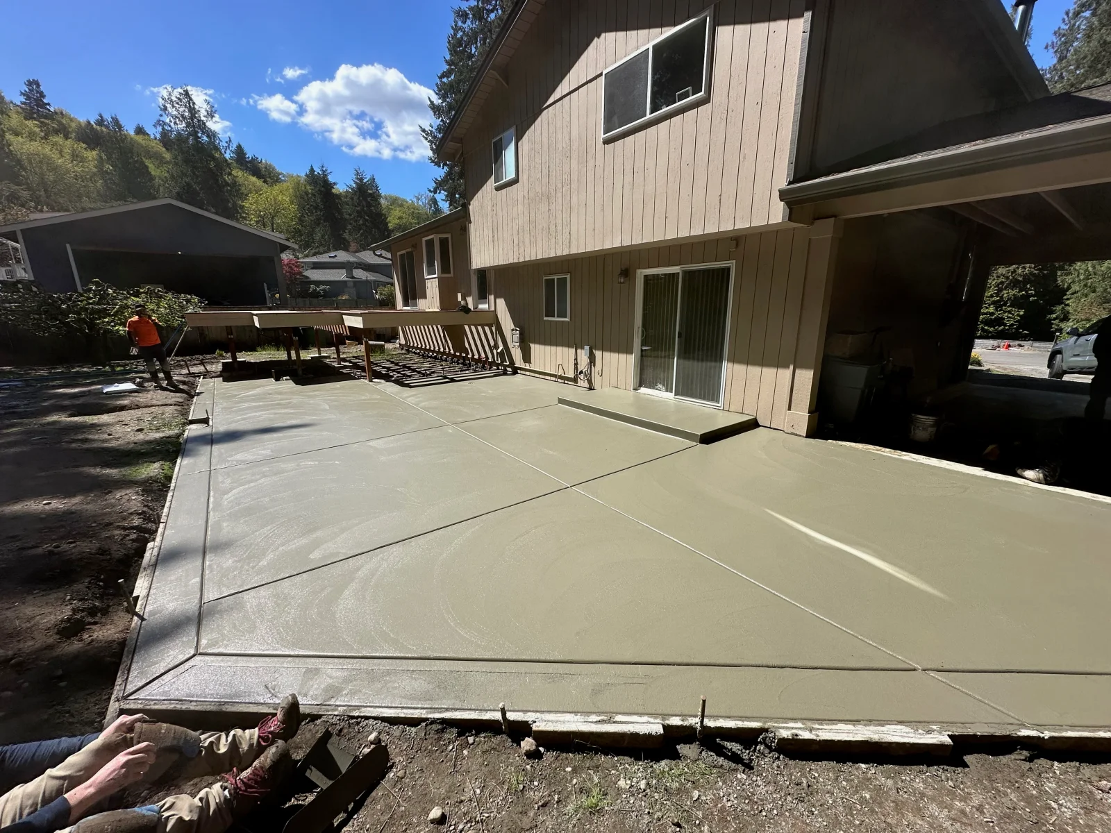 Newly poured concrete patio with control joints, residential home with metal siding in background