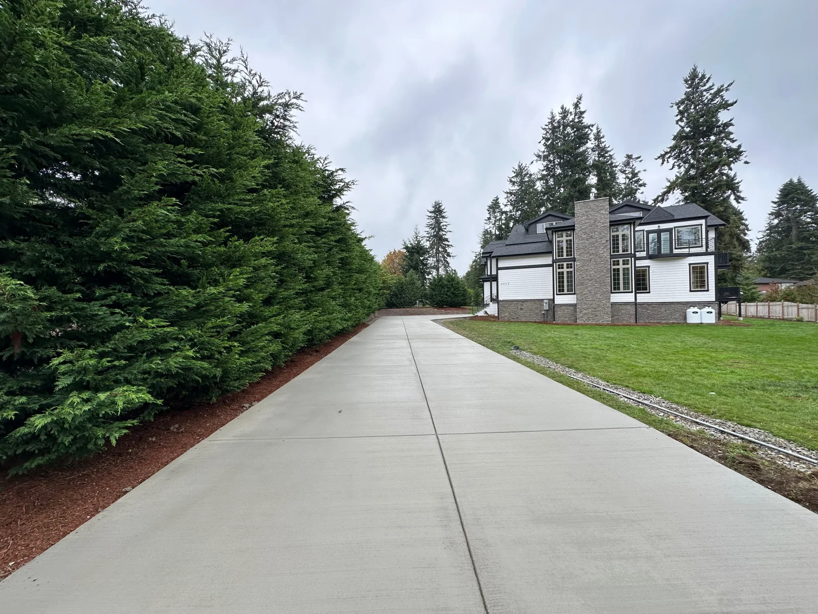 Concrete driveway with control joints, bordered by hedges and lawn