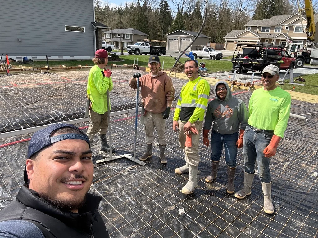 Concrete driveway installation with steel mesh reinforcement and crew on residential property