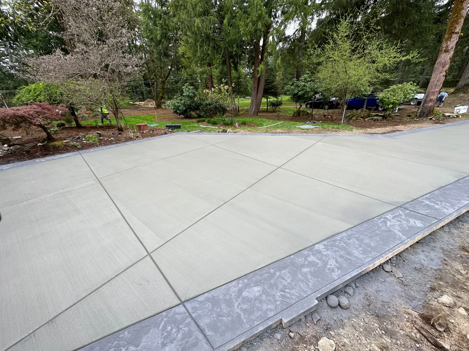 Newly poured concrete driveway with broom finish and dark border edging, control joints visible