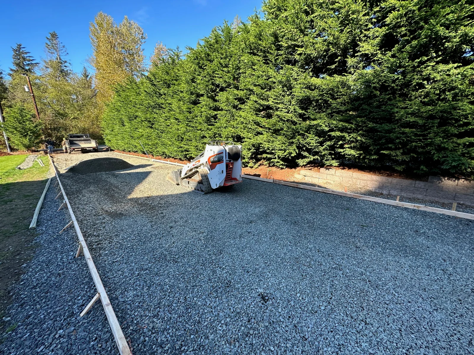 Concrete driveway installation with metal forms, compacted gravel base, and finishing equipment on-site