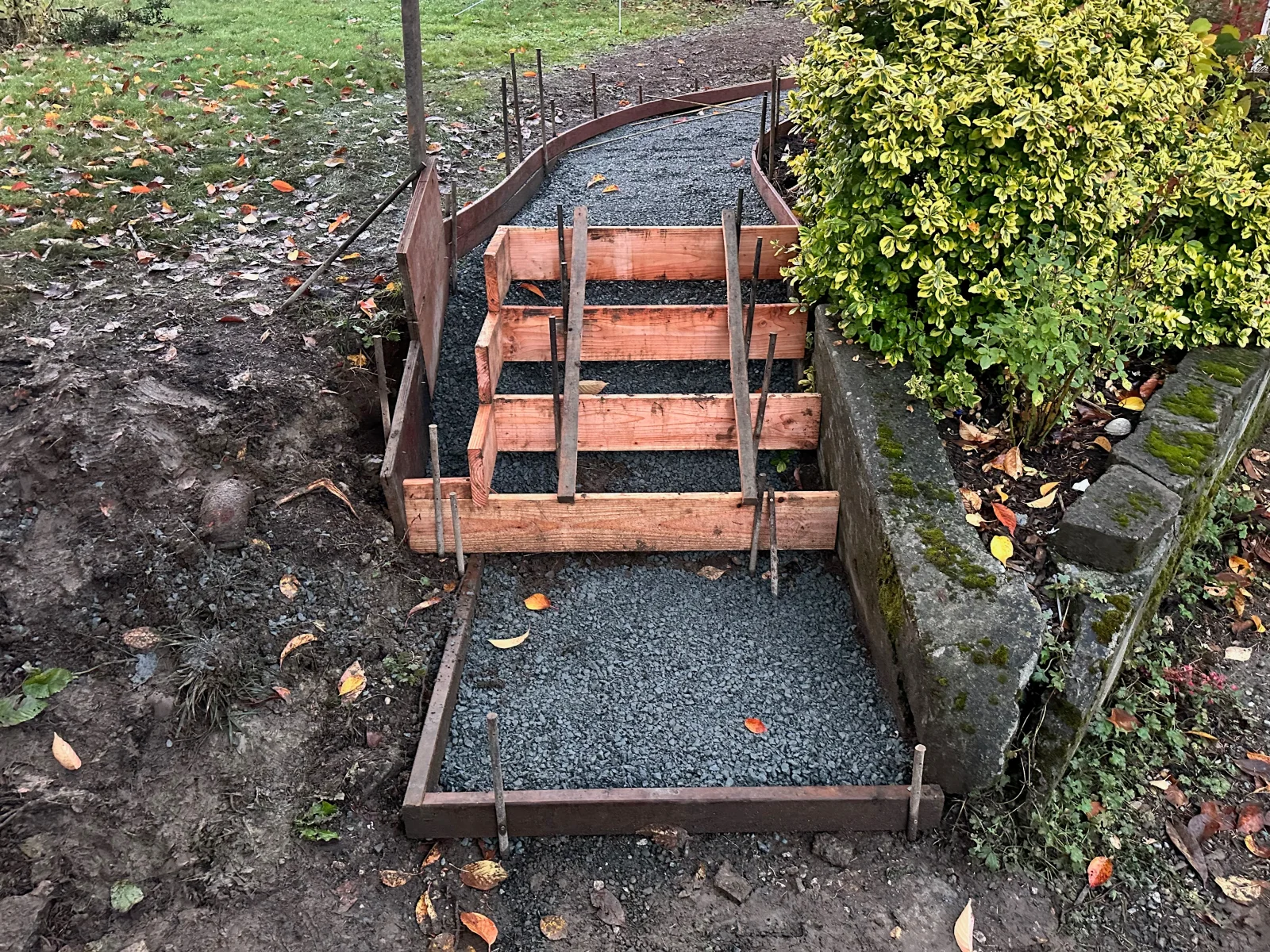 Curved concrete pathway with timber frame edging and gravel base in garden setting