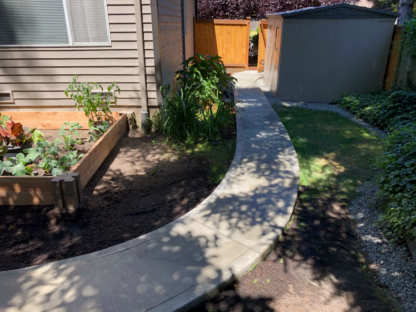 Concrete walkway with broom finish texture alongside raised garden bed and landscaping
