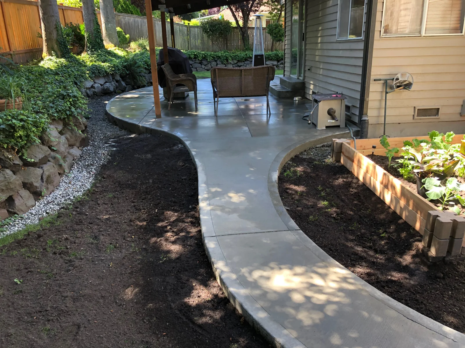 Broom-finished concrete patio and curved walkway with raised garden beds and mature trees