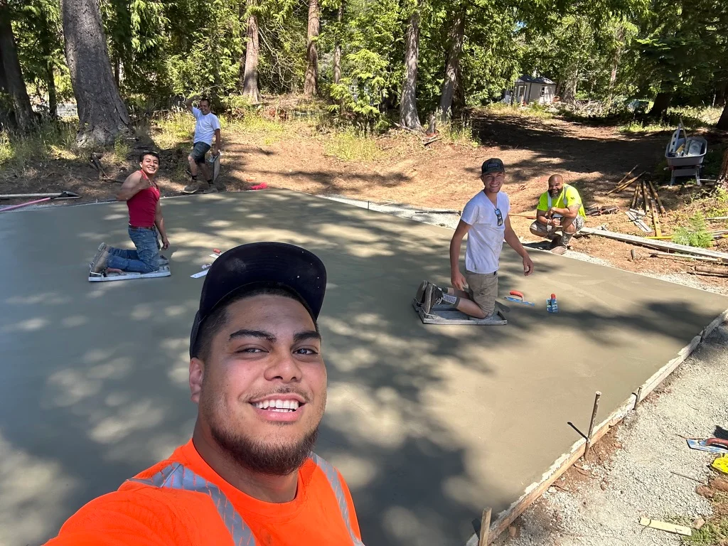 Freshly finished concrete pad with crew members working on site preparation and finishing in wooded area